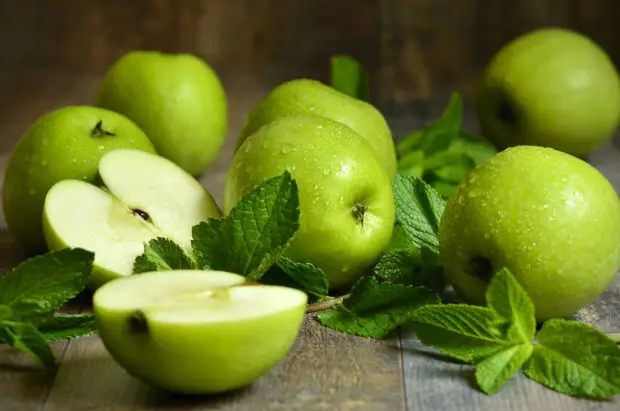 Green apples with mint leaves on wooden table.