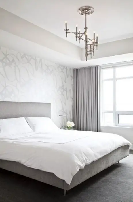 Modern silver gray bedroom with silver metallic wallpaper accent wall, gray linen modern bed, crisp white hotel bedding with white stitching, lilac gray curtains window panels and polished nickel winding Omega Chandelier.
